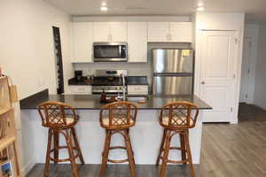 Kitchen with stainless steel appliances, a peninsula, a sink, white cabinetry, and dark countertops