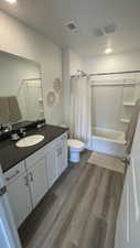 Full bath featuring visible vents, toilet, shower / tub combo with curtain, wood finished floors, and vanity