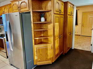 Kitchen with appliances with stainless steel finishes, brown cabinets, light colored carpet, and light tile patterned floors