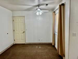 Unfurnished room with ceiling fan, visible vents, dark colored carpet, and baseboards