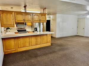 Kitchen with brown cabinetry, appliances with stainless steel finishes, a peninsula, light countertops, and a sink