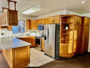 Kitchen featuring brown cabinets, open shelves, stainless steel appliances, light countertops, and a sink