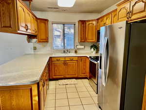 Kitchen featuring light countertops, visible vents, appliances with stainless steel finishes, brown cabinetry, and a sink