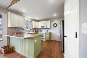 Kitchen featuring dark wood-type flooring, white appliances, a peninsula, and a kitchen breakfast bar