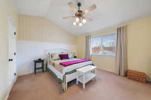 Bedroom with lofted ceiling, ceiling fan, a wainscoted wall, carpet flooring, and wallpapered walls