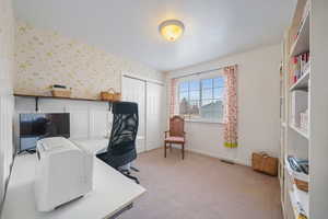 Office area with light carpet, wallpapered walls, visible vents, and baseboards