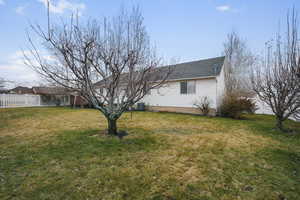 Exterior space featuring a shingled roof, a lawn, cooling unit, and fence