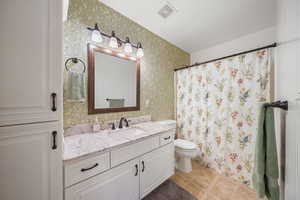 Bathroom with visible vents, wallpapered walls, toilet, vanity, and tile patterned floors