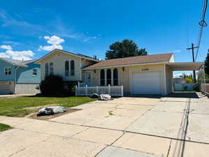 Tri-level home with driveway, a garage, brick siding, a carport, and a shingled roof