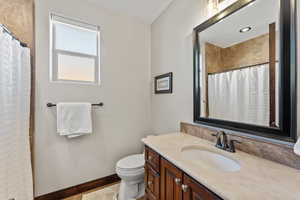 Bathroom featuring curtained shower, vanity, toilet, and baseboards