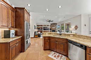 Kitchen with a stone fireplace, light stone counters, a sink, open floor plan, and appliances with stainless steel finishes