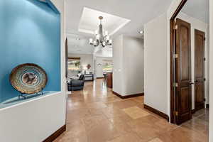 Corridor featuring stone tile floors, baseboards, a raised ceiling, and a notable chandelier