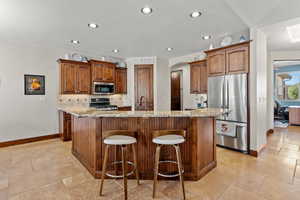 Kitchen featuring an island with sink, light stone countertops, stainless steel appliances, and stone tile flooring