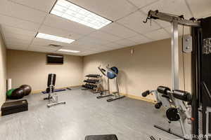 Exercise room with a drop ceiling, wood finished floors, visible vents, and baseboards