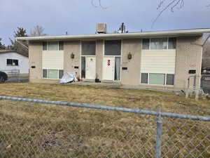 Split foyer home featuring brick siding, fence, central AC, and a front yard