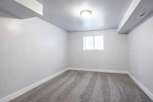 Carpeted spare room featuring visible vents, a textured ceiling, and baseboards