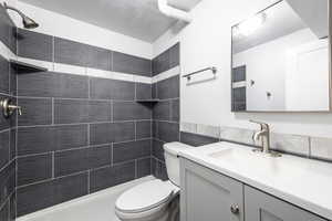 Full bath featuring visible vents, tiled shower, toilet, vanity, and tile walls