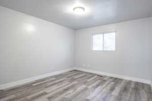 Unfurnished room featuring a textured ceiling, light wood finished floors, and baseboards