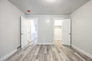 Unfurnished bedroom featuring visible vents, baseboards, light wood-style flooring, a walk in closet, and a textured ceiling