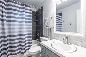 Bathroom featuring vanity, shower / bath combination with curtain, toilet, and decorative backsplash