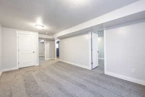 Finished below grade area with carpet, visible vents, a textured ceiling, and baseboards