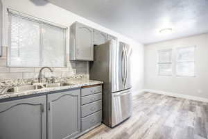 Kitchen featuring tasteful backsplash, freestanding refrigerator, gray cabinetry, light wood-style floors, and a sink