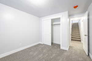 Unfurnished bedroom featuring a closet, light carpet, a textured ceiling, and baseboards