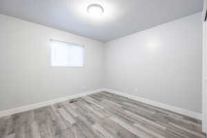 Unfurnished room featuring a textured ceiling, light wood-type flooring, visible vents, and baseboards