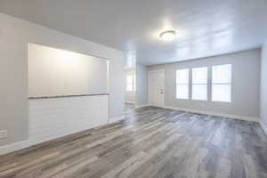 Empty room featuring a textured ceiling, baseboards, and wood finished floors