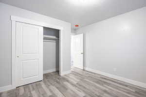 Unfurnished bedroom with a closet, baseboards, a textured ceiling, and light wood finished floors