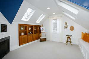 Additional living space with recessed lighting, light colored carpet, baseboards, lofted ceiling with skylight, and a glass covered fireplace