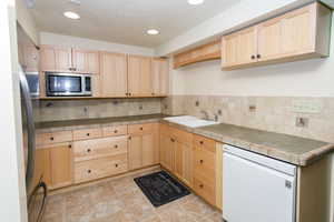 Kitchen featuring stainless steel appliances, light brown cabinetry, and tile counters