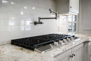 Details with stainless steel gas cooktop, tasteful backsplash, white cabinetry, and light stone countertops