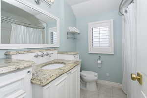 Bathroom featuring tile patterned flooring, toilet, vanity, baseboards, and vaulted ceiling