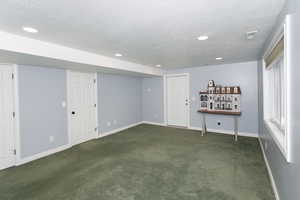 Below grade area with a textured ceiling, dark colored carpet, recessed lighting, and baseboards