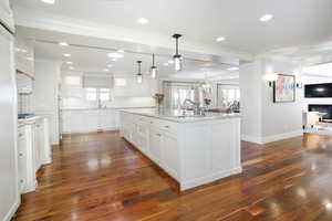 Kitchen with decorative light fixtures, a center island with sink, open floor plan, white cabinetry, and a sink