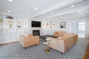 Living room featuring a glass covered fireplace, beamed ceiling, crown molding, light wood-style floors, and recessed lighting