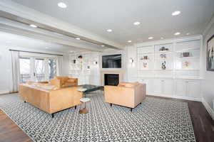 Living room featuring a glass covered fireplace, ornamental molding, beamed ceiling, wood finished floors, and recessed lighting