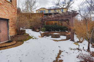 Yard layered in snow featuring an outdoor fire pit and a pergola