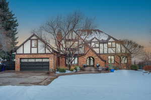 Tudor home with driveway, brick siding, a chimney, and an attached garage