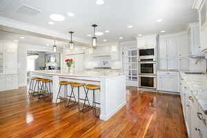 Kitchen featuring built in appliances, a large island, visible vents, and white cabinetry