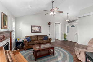 Living area with a textured ceiling, a tile fireplace, a ceiling fan, vaulted ceiling, and dark wood-style floors