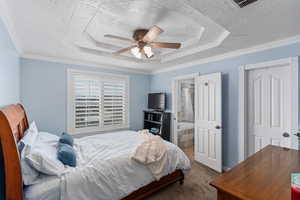 Carpeted bedroom with a textured ceiling, ornamental molding, and a raised ceiling