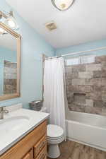 Full bathroom with toilet, wood finished floors, vanity, visible vents, and shower / tub combo with curtain