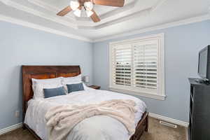 Bedroom with a raised ceiling, visible vents, dark carpet, and baseboards