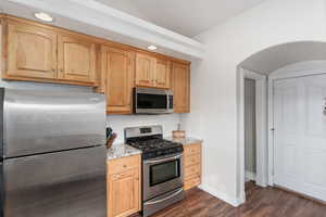 Kitchen with light stone counters, arched walkways, dark wood-style floors, stainless steel appliances, and decorative backsplash