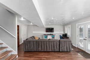 Living area with a textured ceiling, french doors, dark wood-style flooring, and stairway