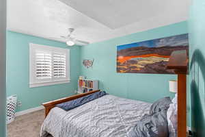 Carpeted bedroom featuring ceiling fan, baseboards, and a textured ceiling