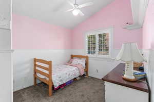 Bedroom with lofted ceiling, a wainscoted wall, a ceiling fan, and carpet flooring