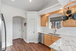 Kitchen with vaulted ceiling, a sink, light stone countertops, dishwasher, and fridge